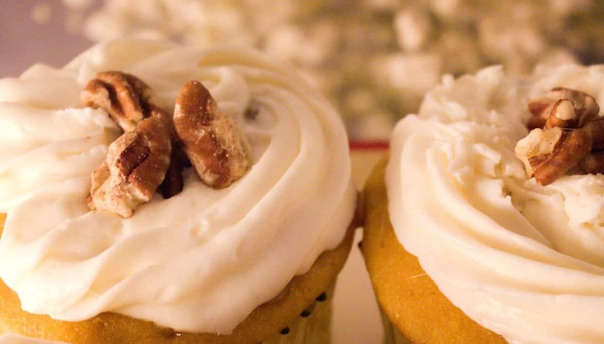 Two cupcakes topped with white frosting and garnished with pecan pieces, displayed close together.