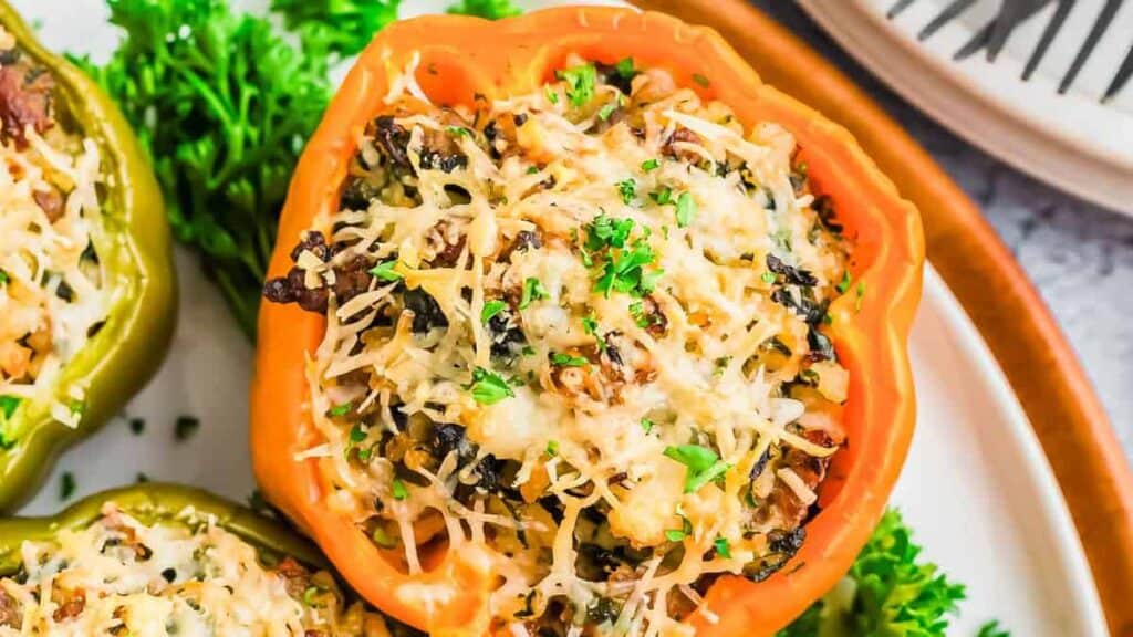 Close-up of a stuffed bell pepper filled with a mixture of rice, vegetables, and topped with melted cheese and parsley, served on a white plate with a decorative napkin in the background.