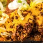 A close-up of cheesy taco casserole with ground beef, topped with melted cheese, shredded lettuce, and a dollop of sour cream.