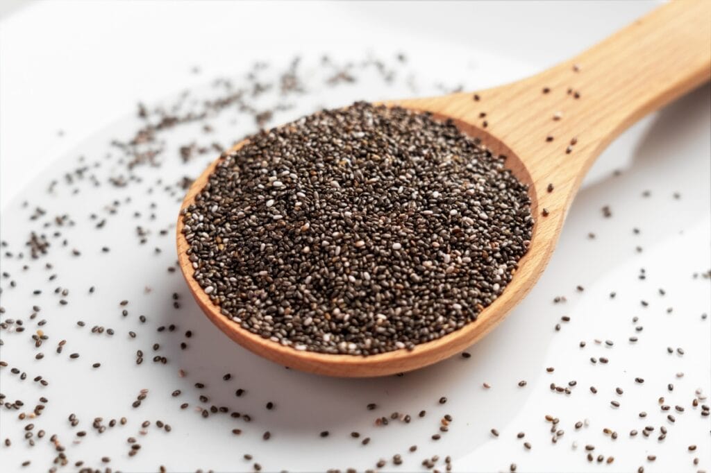 A wooden spoon filled with chia seeds, resting on a white surface with additional scattered seeds.