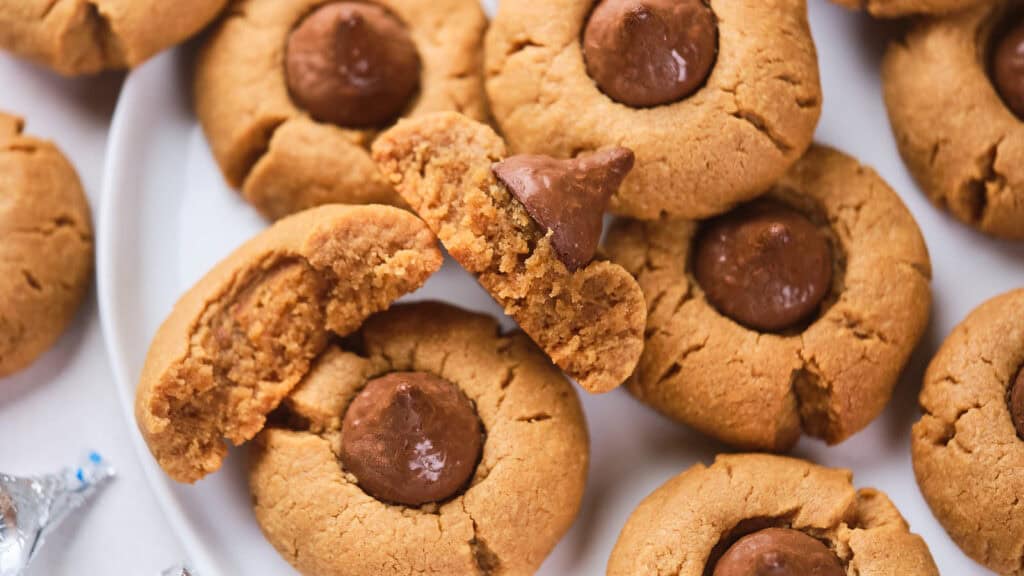 A plate of peanut butter cookies with chocolate kisses in the center, some cookies are whole and one is broken in half.