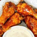 A plate of glazed chicken wings is arranged next to a small bowl of dipping sauce. The wings are golden-brown and appear to be seasoned.