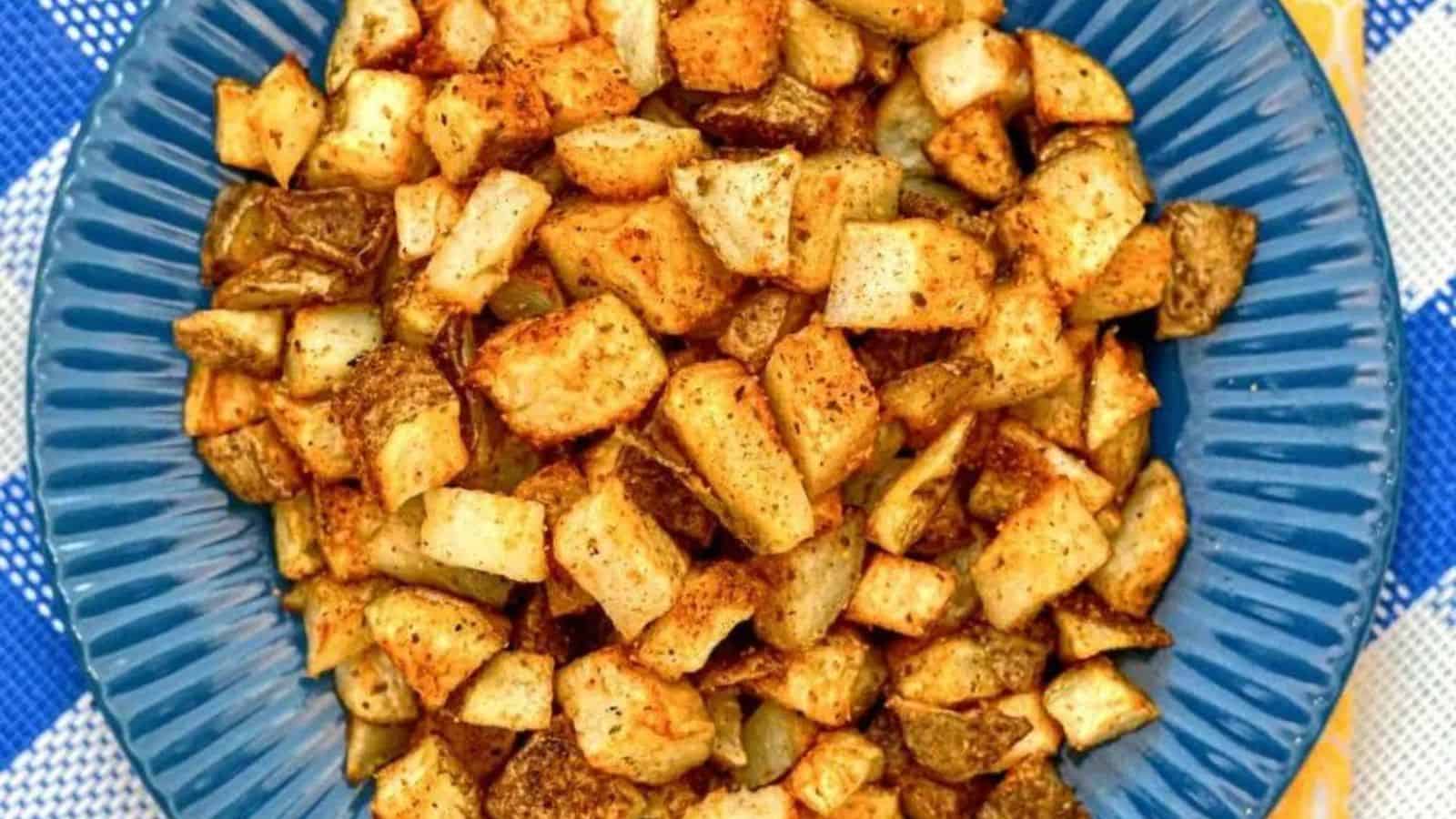 Golden diced potatoes in a white bowl with a sprinkle of herbs and seasoning.