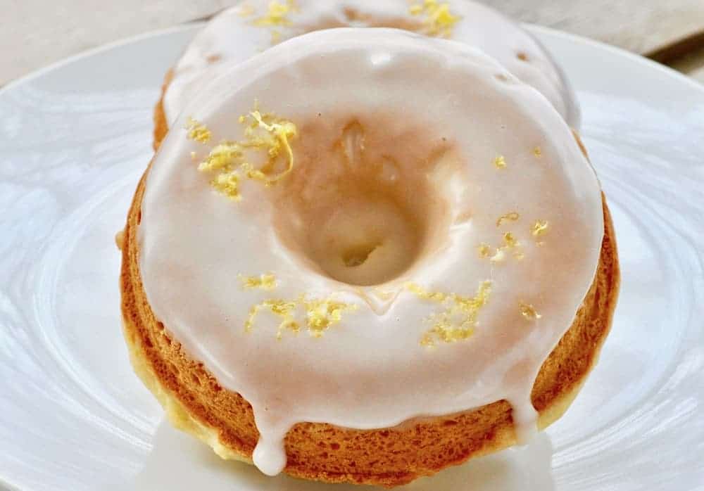 Two glazed donuts with a lemon zest topping are placed on a white plate.