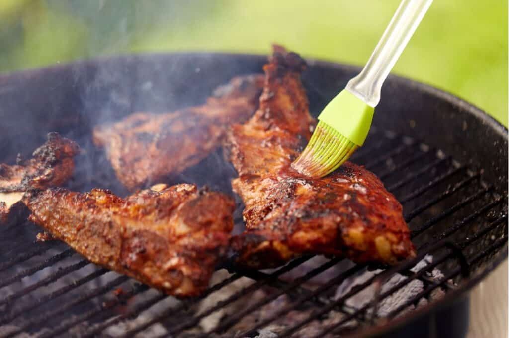 Barbecue ribs being brushed with sauce on a grill.