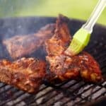 Barbecue ribs being brushed with sauce on a grill.