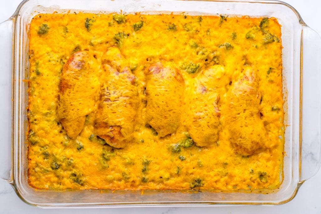 A baked dish with a layer of melted cheese on top, containing pieces of chicken and visible broccoli florets, served in a rectangular glass baking dish.