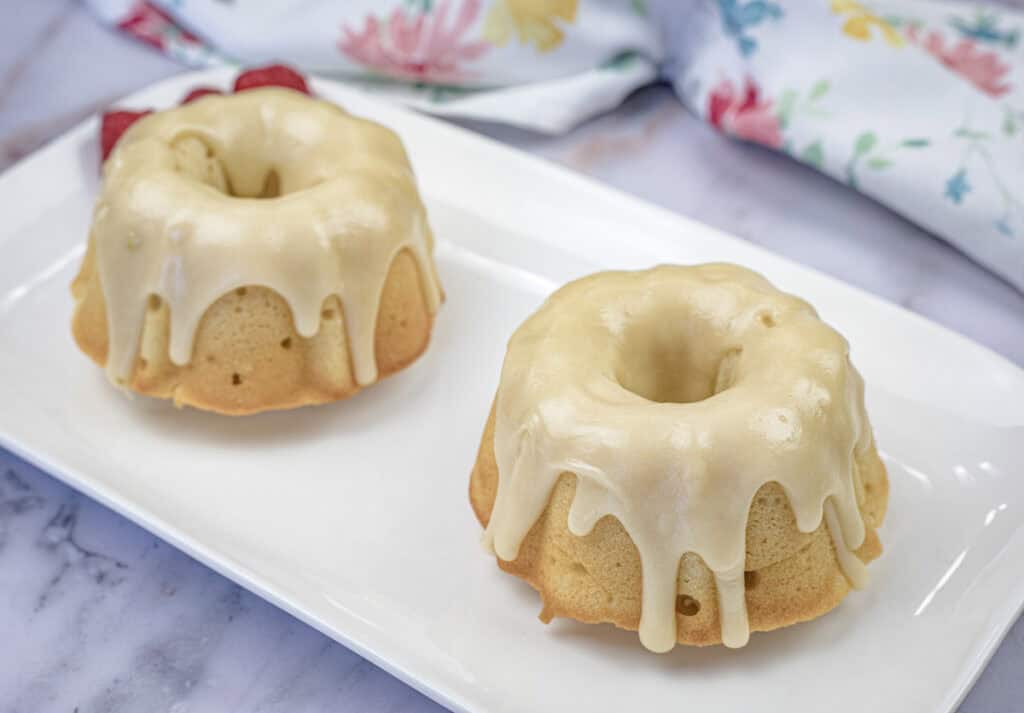 Two small Bundt Grandma's Buttermilk Cake with a smooth white glaze sit on a rectangular white plate.