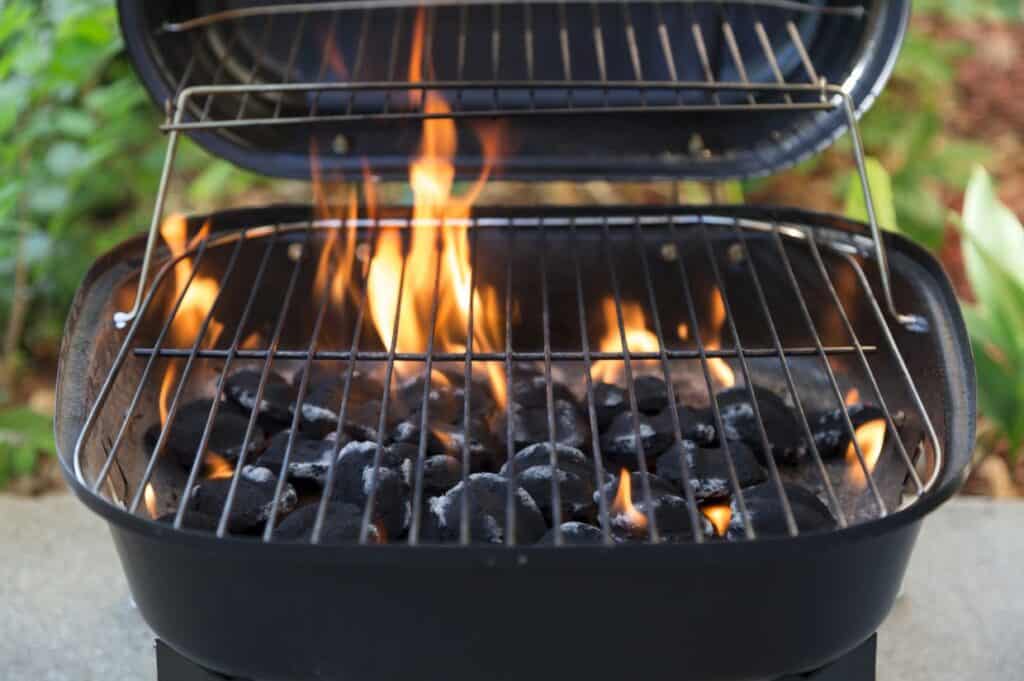 A charcoal grill with flames and hot coals is ready for cooking outdoors, perfect for trying out some grilling tips for beginners.