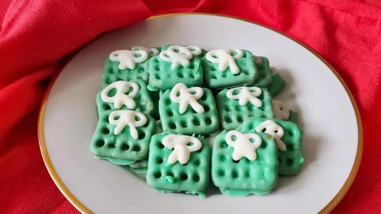 A plate of square-shaped green cookies with white icing decorations, arranged neatly, with a red cloth backdrop.