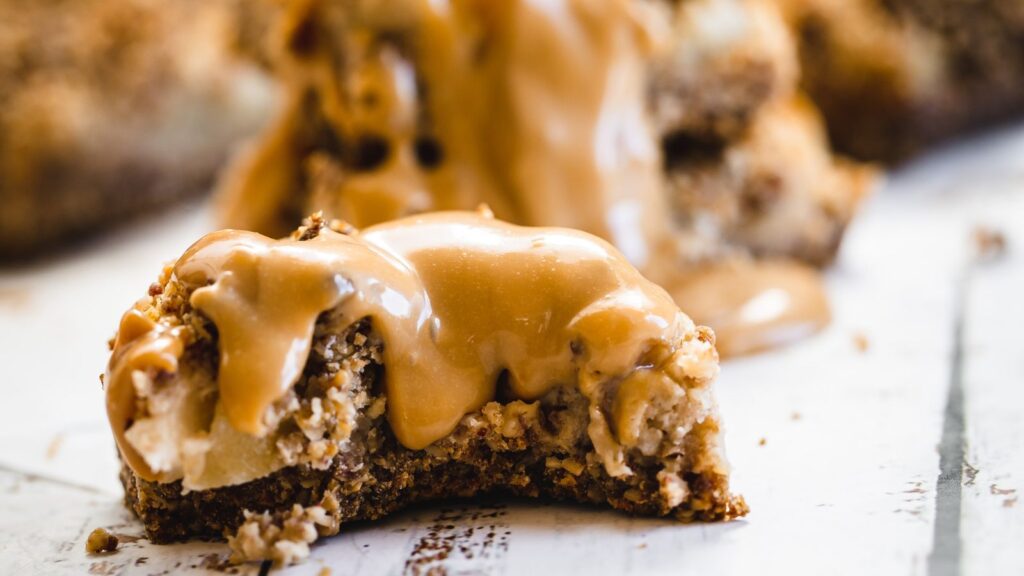 A close-up of a partially eaten pastry topped with a thick layer of caramel sauce on a white, weathered surface.