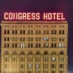 The exterior of Congress Hotel at night, with "CONGRESS HOTEL" illuminated in red neon lights on the roof of the building.