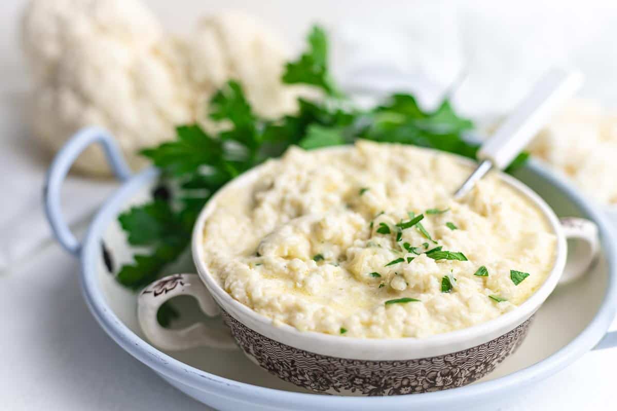 A bowl filled with cauliflower mash garnished with fresh parsley.