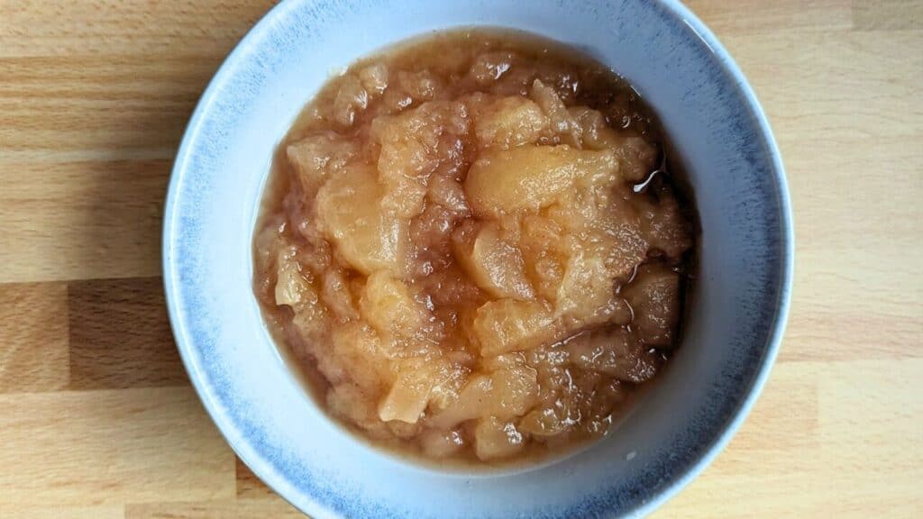 A bowl of chunky applesauce on a wooden surface.