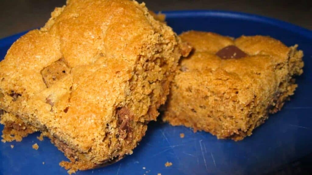 Two square pieces of golden-brown cookie bars with visible chocolate chunks, served on a blue plate.