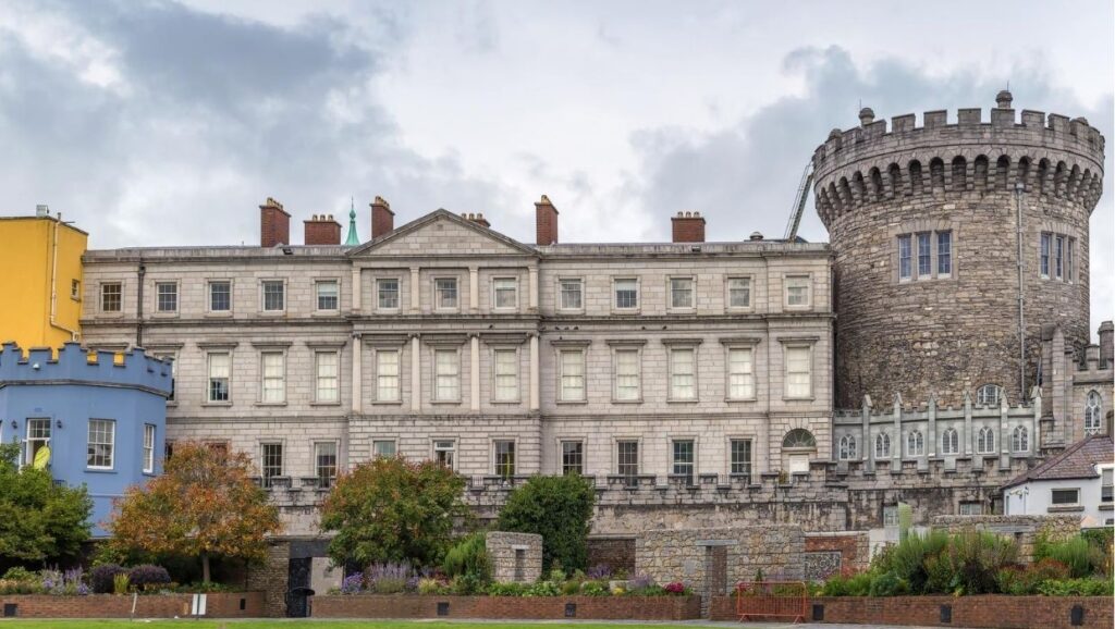 Historic building with classical and medieval architectural elements, featuring a round tower and a symmetrical facade. Surrounding vegetation and a cloudy sky provide a contrasting backdrop, making it an essential stop on any 4 day Ireland itinerary.