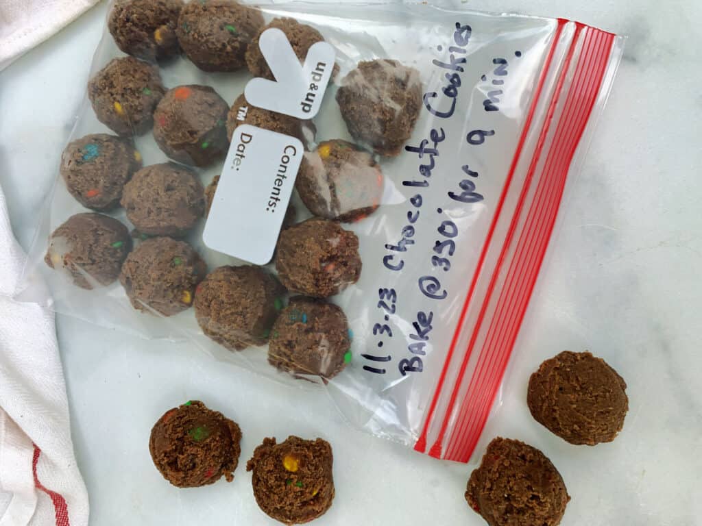 A ziplock bag labeled with instructions contains cookie dough balls, with some cookie dough balls placed outside on a countertop.