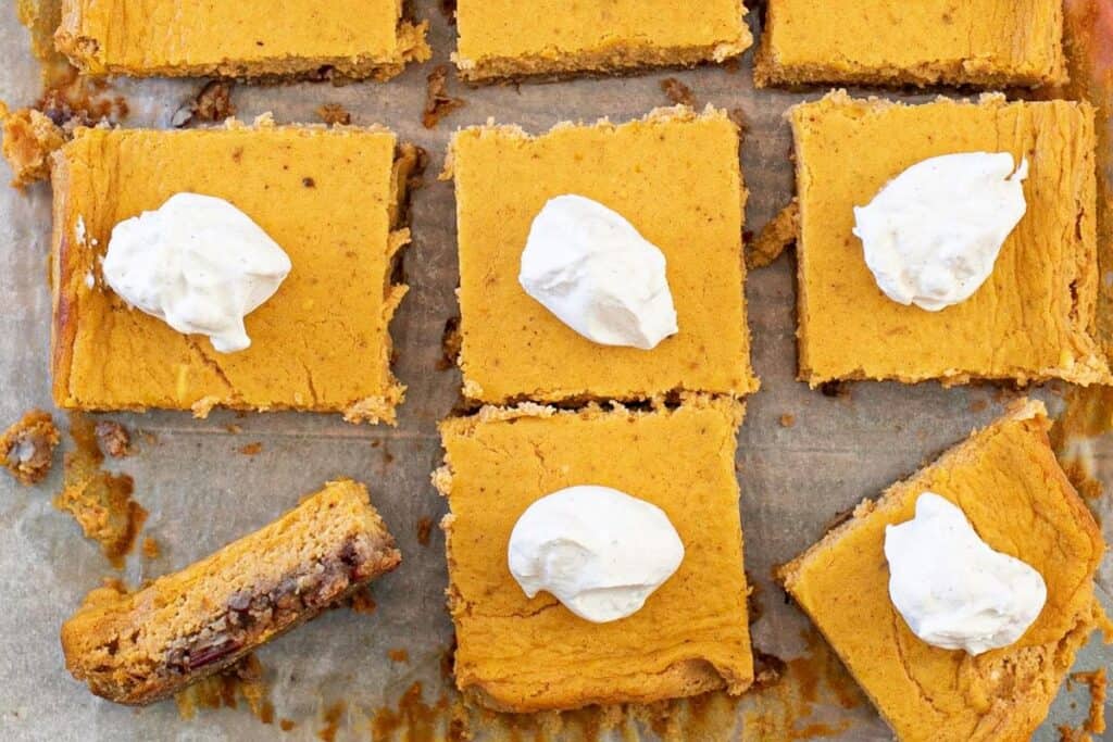 Eight squares of pumpkin dessert topped with dollops of whipped cream, with one additional square partially eaten.