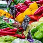 A colorful display of various peppers, including red, yellow, green, and orange, arranged neatly at a market stall with price tags showing.