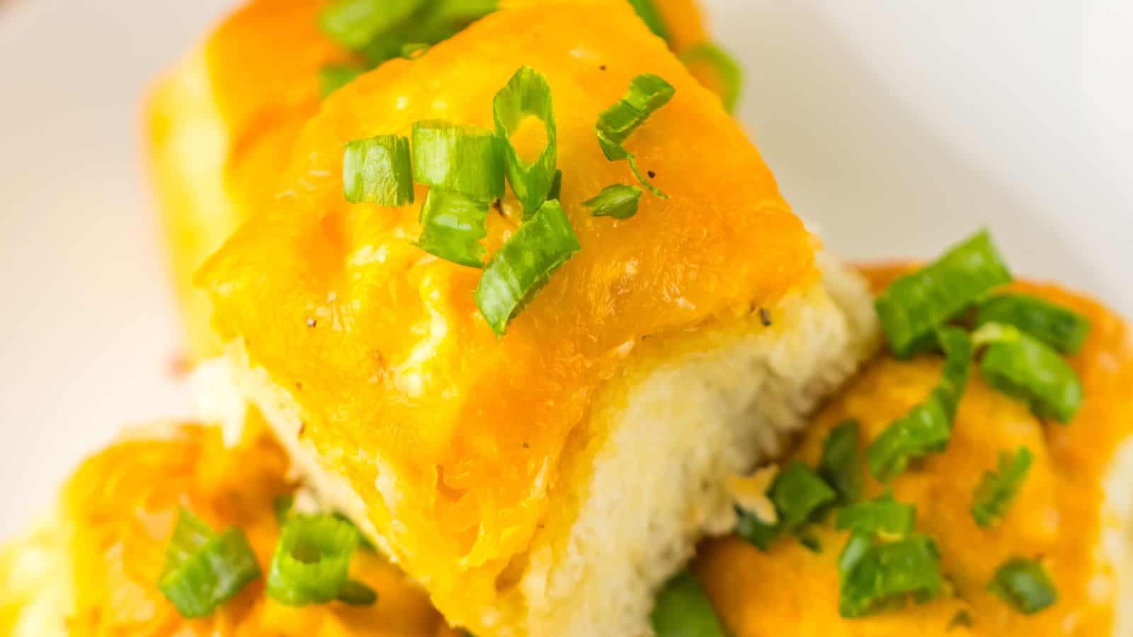 Close-up of cheesy garlic bread rolls topped with chopped green onions on a white plate, reminiscent of Loaded Buffalo Chicken Rolls.