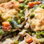 Close-up of a chicken pot pie filled with peas, carrots, and chunks of chicken, topped with golden-brown biscuit pieces.