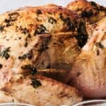 A roasted turkey seasoned with herbs, presented on a clear glass platter.