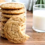 A stack of homemade cookies tied with a string, with one cookie showing a bite taken out of it, and a glass of milk on a wooden table.