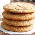 A stack of four snickerdoodle cookies on parchment paper with a glass of milk in the background.