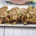 Oven-baked ribs with onion and garlic on top served on a white rectangular plate.