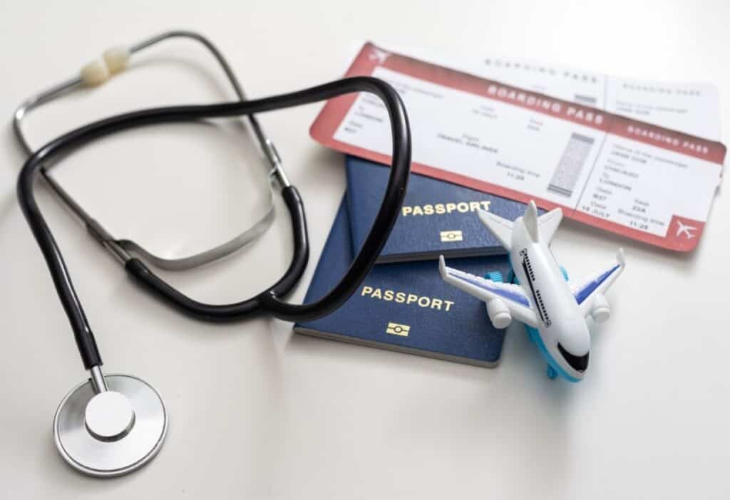 A stethoscope, two passports, a small airplane model, and two boarding passes are arranged on a white surface.