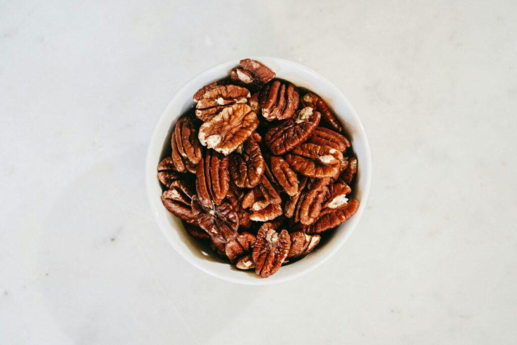 A white bowl filled with pecan nuts on a light-colored surface.