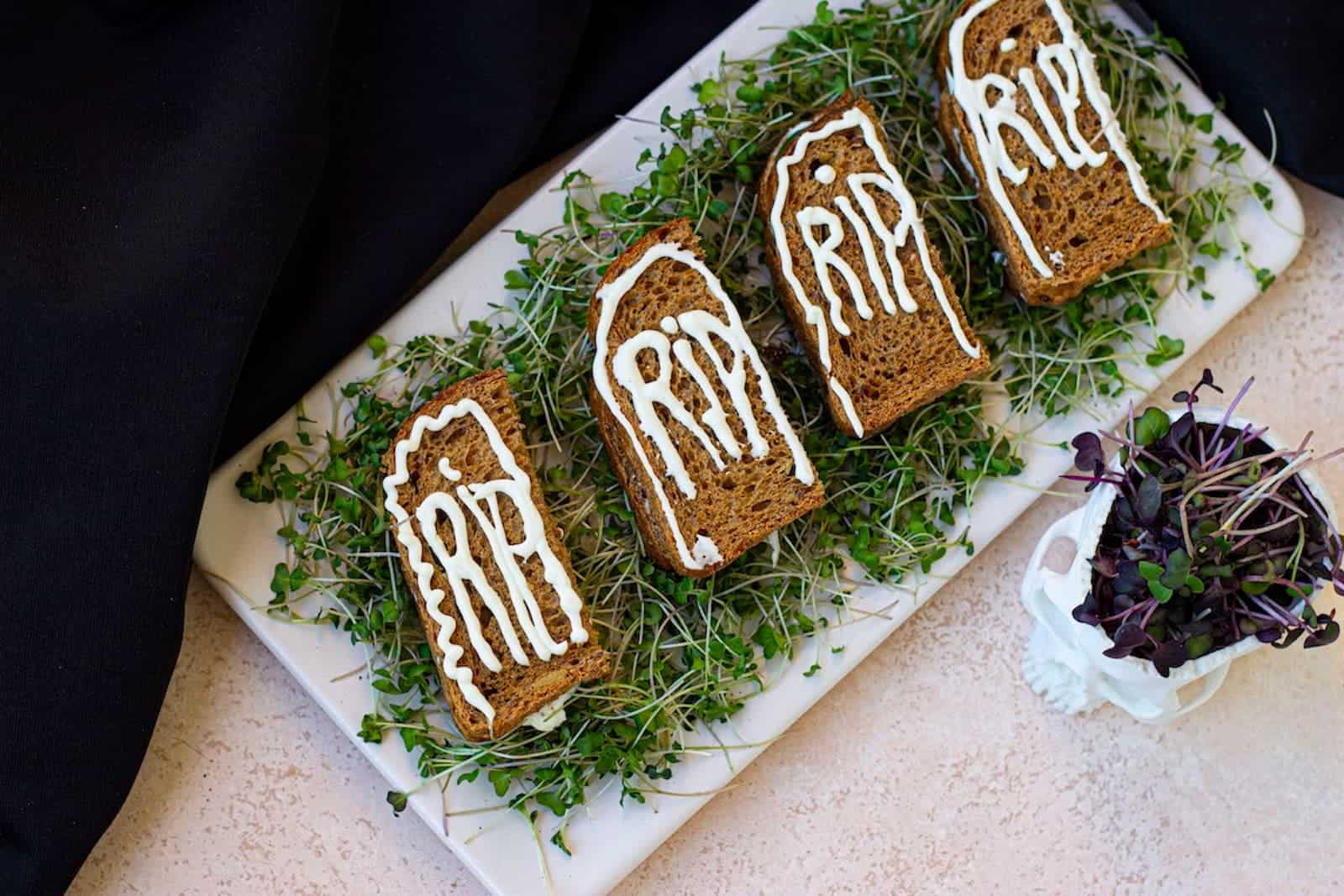 A white plate with four tombstone Halloween sandwiches on it.