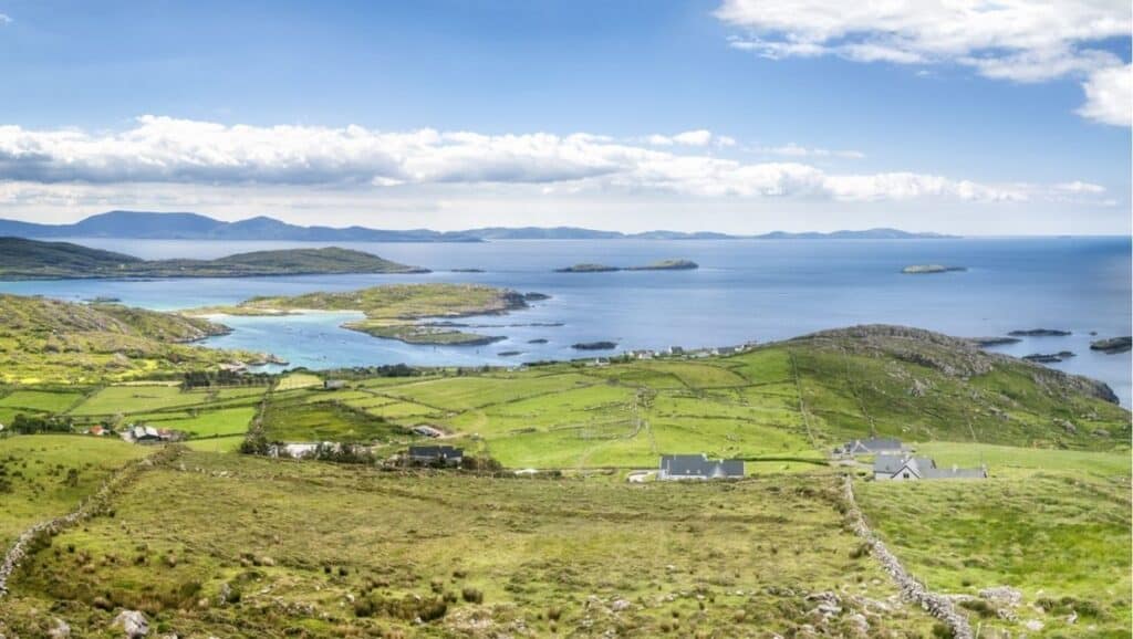 A scenic view of grassy fields, small houses, and islands leading to a blue sea under a partly cloudy sky—perfect for your 4-day Ireland itinerary.