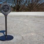 A sign at Arlington National Cemetery reads "Silence and Respect" on a stone-paved area, with grave markers and bare trees visible in the background, serving as a poignant reminder of Arlington National Cemetery facts.