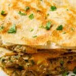 Close-up of layered quesadillas filled with a savory mixture, garnished with chopped fresh parsley.