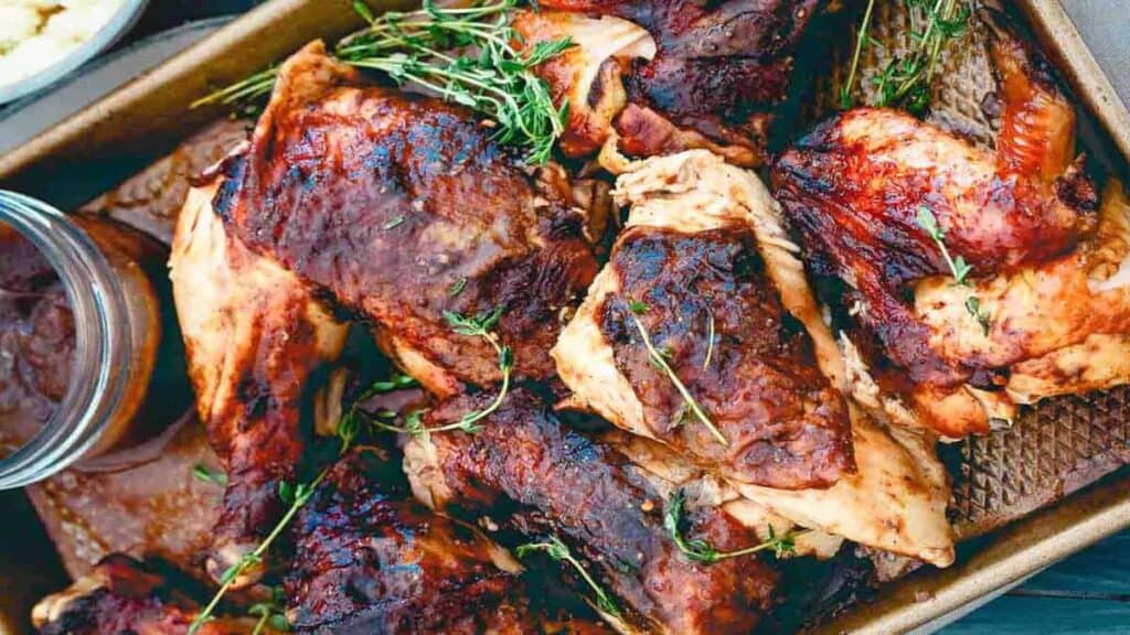 A tray of roasted chicken pieces, some with crispy browned skin, garnished with fresh herbs.