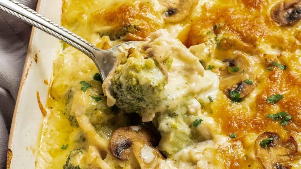 A close-up of a creamy broccoli and mushroom casserole being served with a spoon.