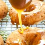 Caramel is being drizzled over freshly baked donuts placed on a cooling rack.