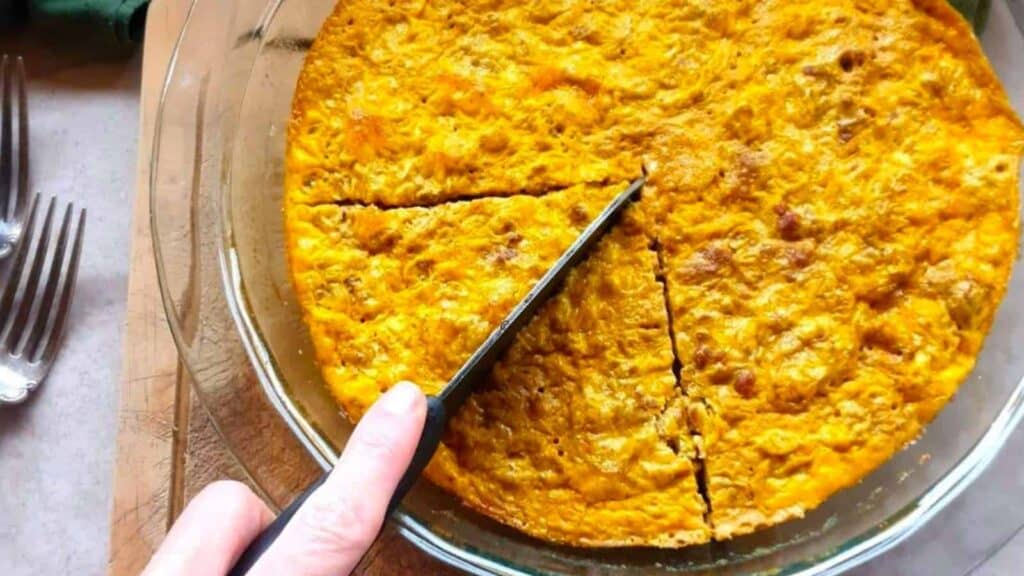 A knife cutting into a baked, golden-brown dish in a glass pie pan, with three triangular slices already made. Forks are visible on the side, ready for a delightful dinner.