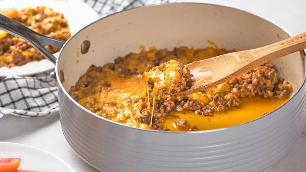 A wooden spoon scoops a portion of cooked ground meat with melted cheese from a pan.