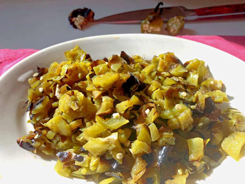 A plate of roasted and chopped green bell peppers with seeds, displayed on a white surface. A knife and pepper remnants are visible in the background.