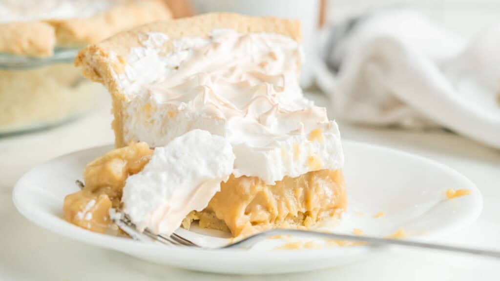 A slice of butterschot pie on a white plate with a fork. The pie filling appears to be a light, creamy texture.