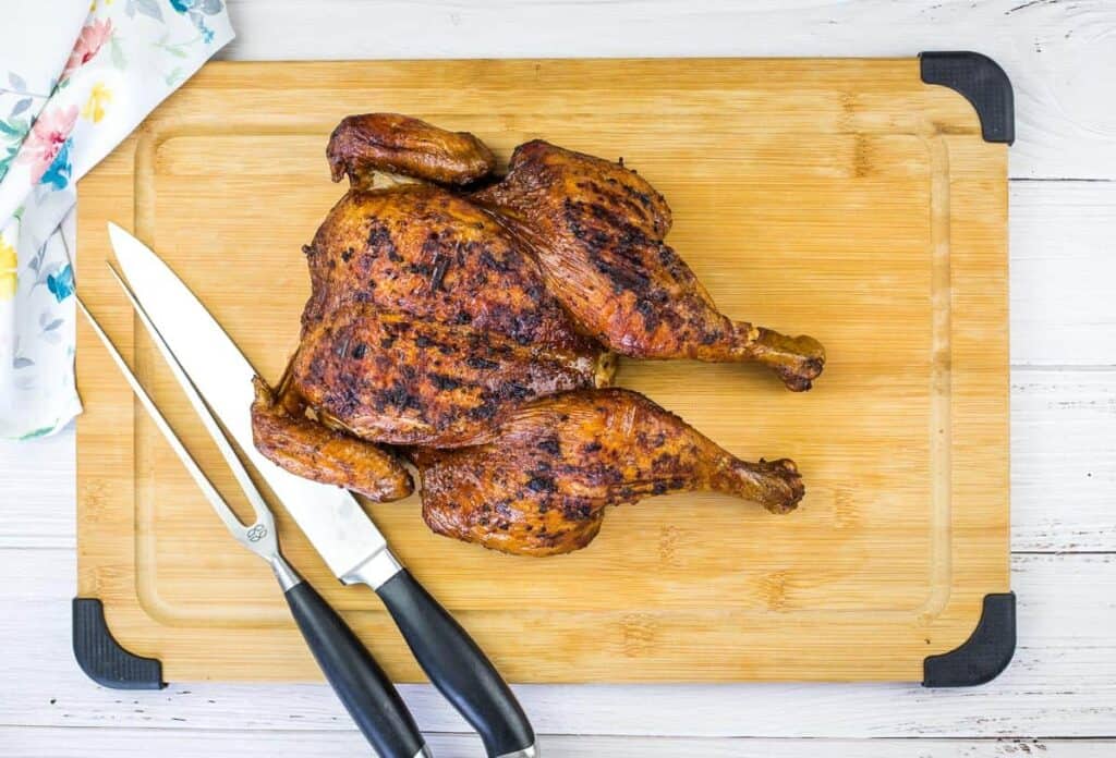 Smoky Whole Chicken on a wooden cutting board with a chef's knife and carving knife beside it, making a perfect addition to your backyard BBQ menu.