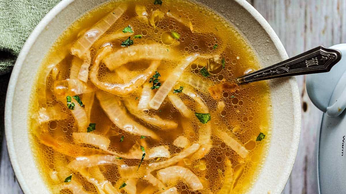 A bowl of onion soup garnished with parsley, with a spoon placed inside the bowl.