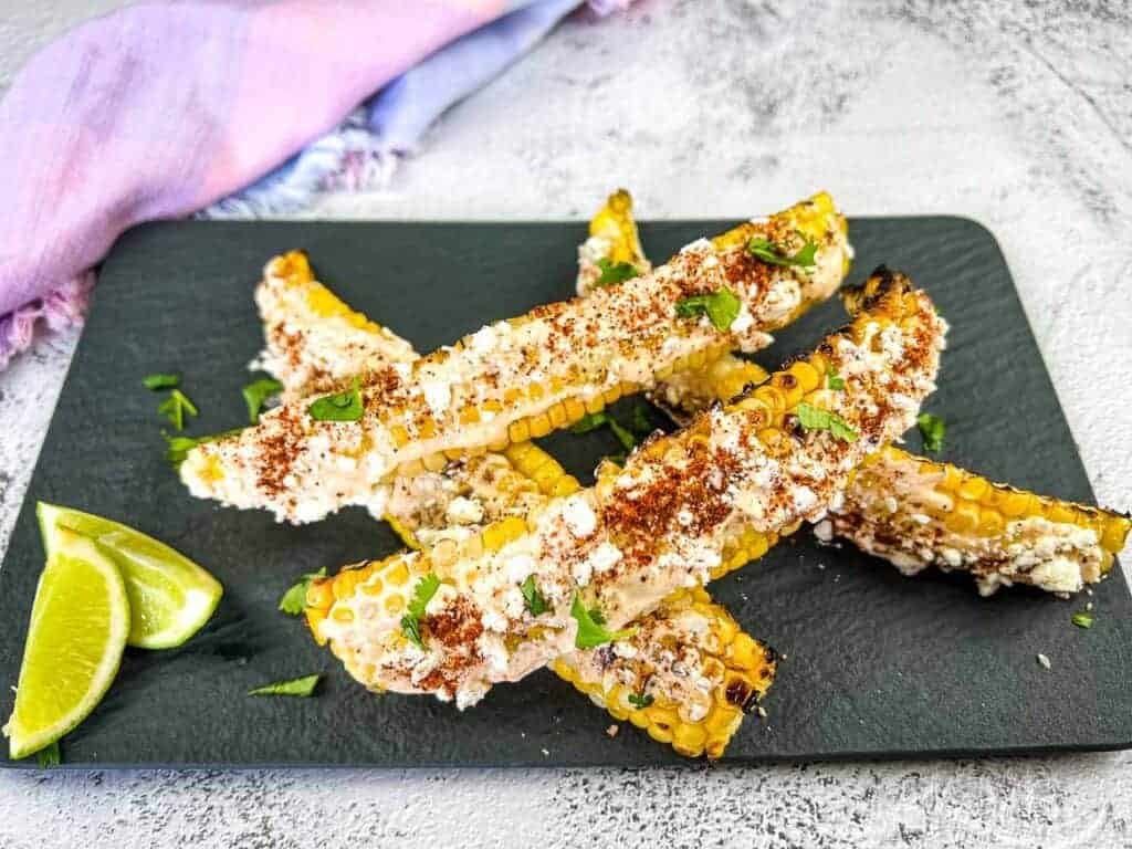 Grilled Elote Corn Ribs  served on a black plate with lime wedges—a perfect addition to your backyard BBQ menu.