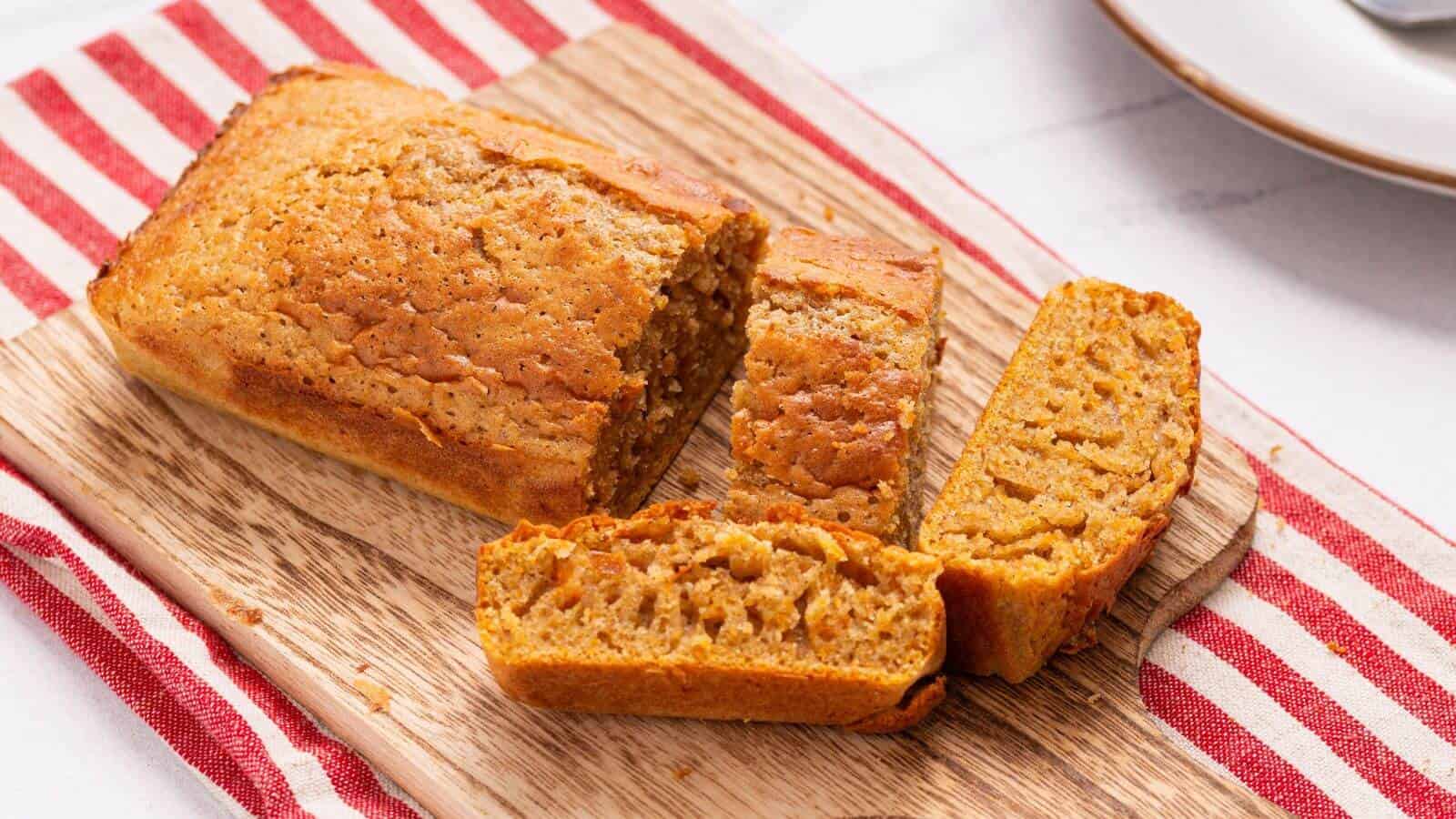 A loaf of sliced pumpkin bread on a wooden cutting board with a red and white striped cloth beneath.