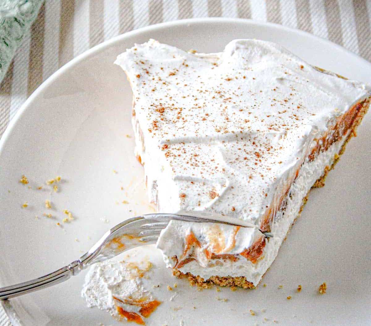 A slice of no-bake pumpkin cheesecake delight on a white plate, partially eaten with a fork resting on the plate.