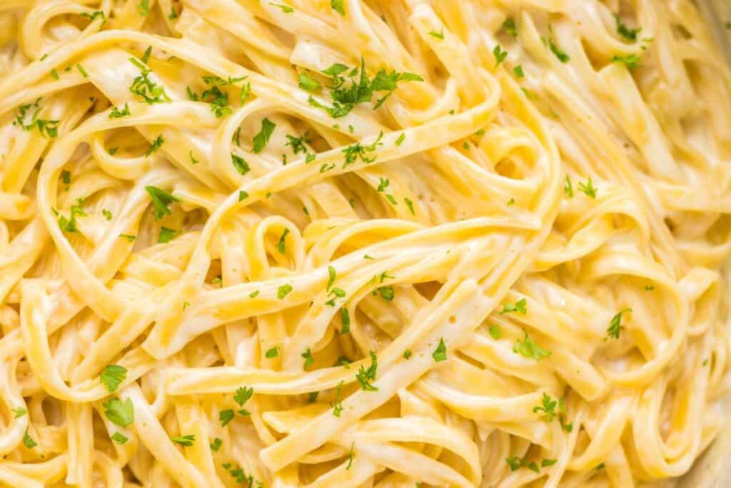 Close-up of fettuccine pasta coated in a creamy Alfredo sauce, garnished with chopped parsley.