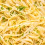 Close-up of fettuccine pasta coated in a creamy Alfredo sauce, garnished with chopped parsley.