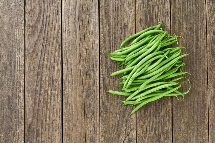 A pile of green beans on a wooden surface.